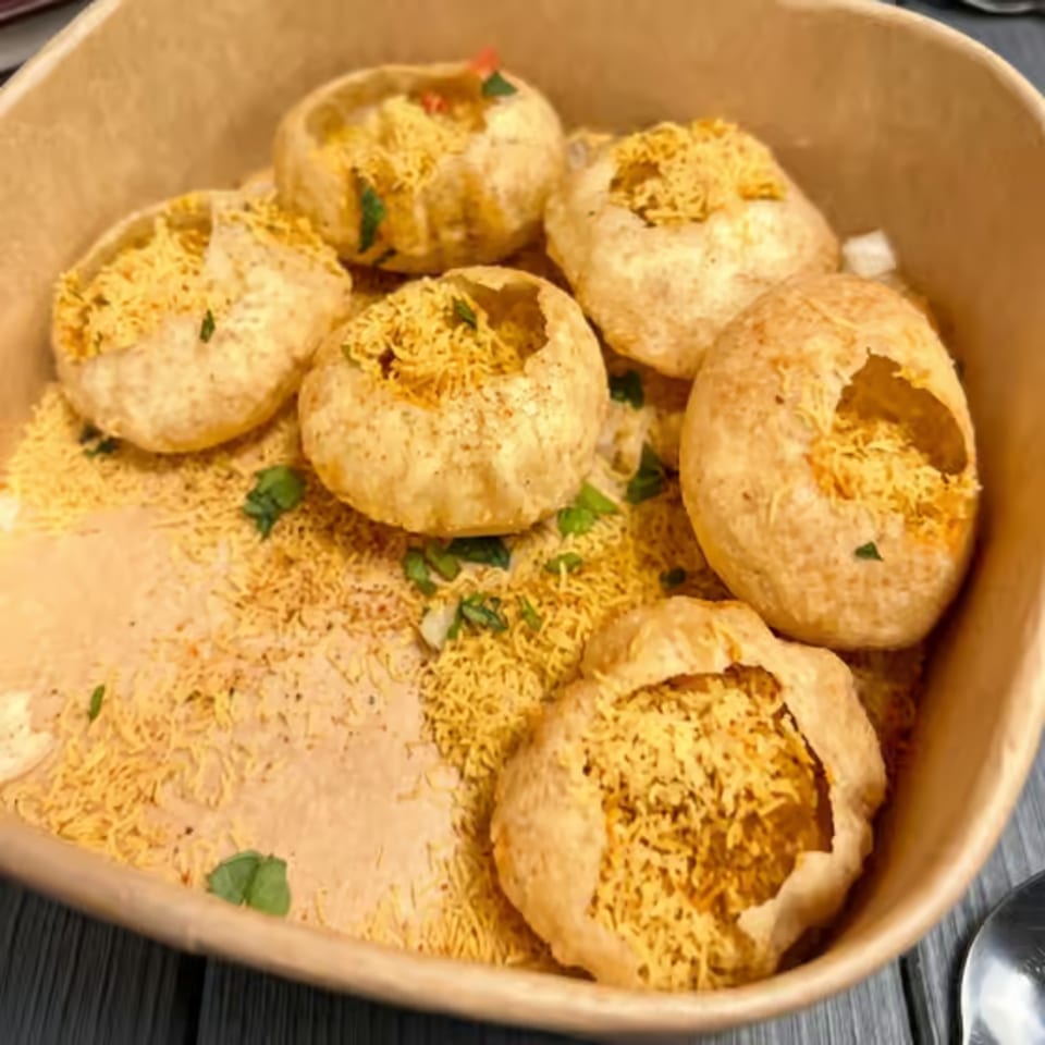 A bowl of pani puri, crispy hollow balls filled with spiced potatoes and chickpeas, topped with sev.
