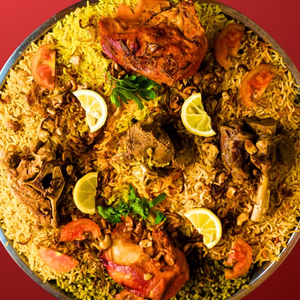 Large platter of Mandi rice with roasted chicken, lamb, lemon, tomatoes, and parsley.