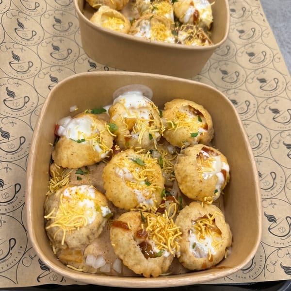 Two bowls of Dahi Puri, topped with yogurt, chutney, and sev, on a Chai Cafe branded paper.