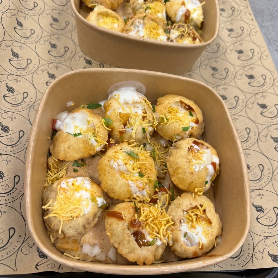 Two bowls of Dahi Puri, topped with yogurt, chutney, and sev, on a Chai Cafe branded paper.
