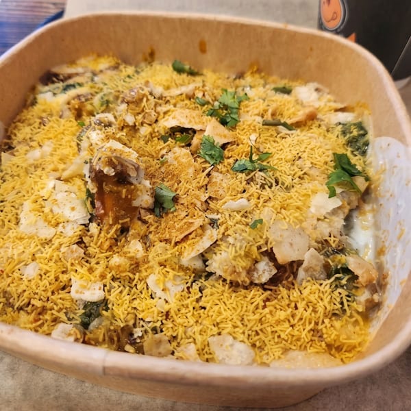 Close-up of a bowl of Indian chaat, topped with crispy sev, spices, and fresh cilantro.